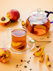 Fresh peach tea in a mug and glass teapot on a yellow-pink background with copy space.