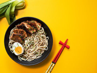 A bowl of ramen chicken soup with egg and sticks on yellow background.