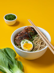 A bowl of ramen chicken soup with egg and sticks on yellow background.