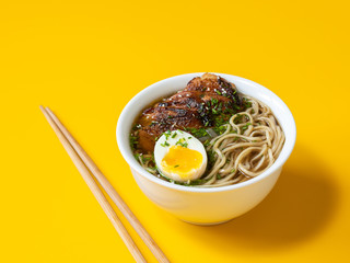 A bowl of ramen chicken soup with egg and sticks on yellow background.