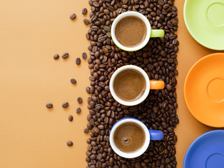 Colored cups of coffee with coffee beans on a brown background.