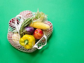 Vegan vegetarian food in a cotton bag. Vegetables and fruits on a green background. Grocery shopping food and zero waste concept.