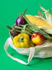 Vegan vegetarian food in a cotton bag. Vegetables and fruits on a green background. Grocery shopping food and zero waste concept.