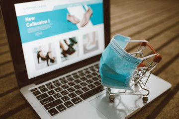 Trolley shopping cart wearing protective mask on a computer laptop keyboard. Concept for shopping online or e-commerce from internet for Coronavirus COVID-19 disease protection.