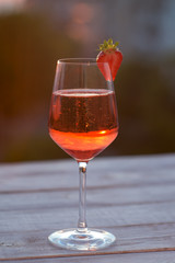 A glass of champagne on the blurred natural background of the sunset. A glass of pink sparkling wine close-up on a white wooden background. Festive evening. Soft focus, beautiful bokeh.