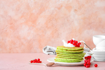 Plate with tasty green pancakes and berries on color background