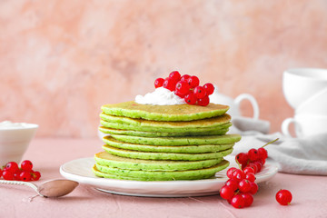 Plate with tasty green pancakes and berries on color background