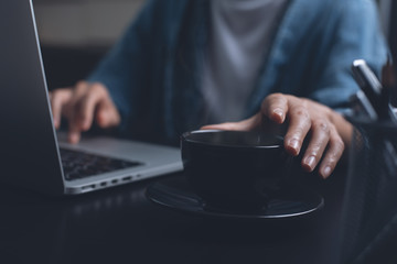 Woman drinking coffee while overtime working on laptop computer at night at home office