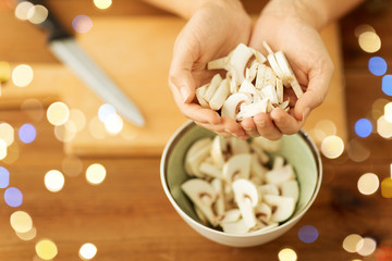 cooking, culinary and edible mushrooms concept - close up of woman holding chopped champignons