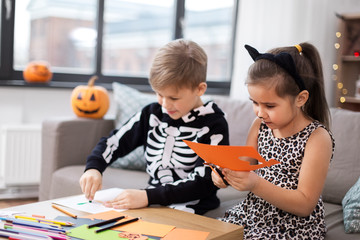 halloween, holiday and childhood concept - smiling little boy and girl in party costumes doing...