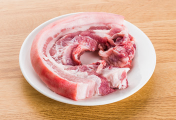 raw pork belly meat put on a plate, isolated on wooden background.