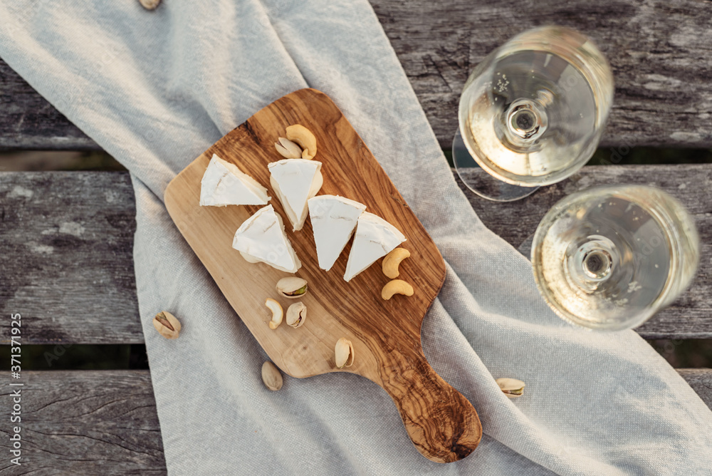 Canvas Prints two glasses of white wine and wooden plate with cheese and nuts during sunset time outside.