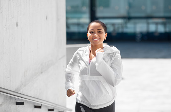 fitness, sport and healthy lifestyle concept - happy smiling young african american woman running upstairs outdoors