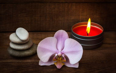 Spa stones with a pink Orchid and a burning candle on a brown wooden background