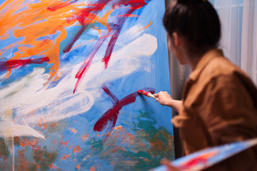 Young artist in art workshop using red paint on large canvas to create a contemporary painting. Modern artwork paint on canvas, creative, contemporary and successful fine art artist drawing