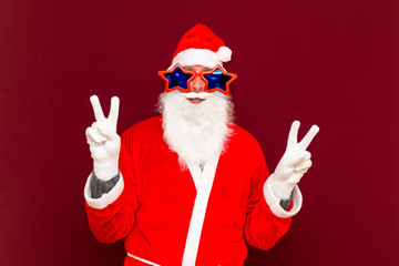 Close up joyful funny playful naughty santa showing peace victory signs, fooling around, in trendy specs, so confident.