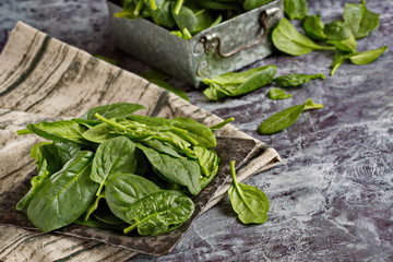 Fresh bright green young spinach leaves lie in a metal box on an old concrete table. Healthy food....