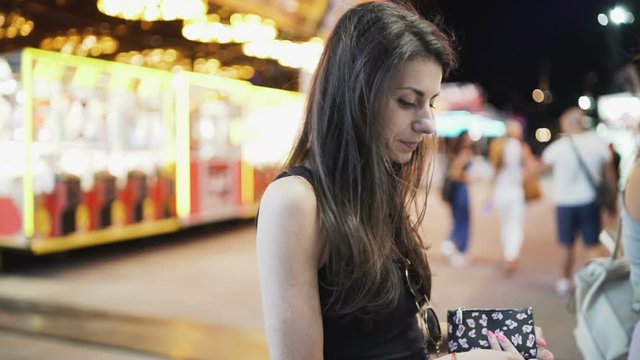 Brunette woman counting cash, waiting on the line to buy carnival tickets 