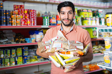 Smiling positive male is posing with purchases near shelves in supermarket.