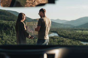 Traveler Couple on a Road Trip, Man and Woman Using Map on Journey Near Their Car Over Beautiful Landscape