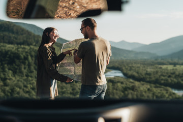 Traveler Couple on a Road Trip, Man and Woman Using Map on Journey Near Their Car Over Beautiful Landscape