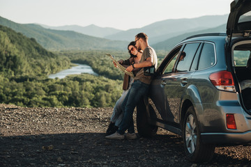 Travelers Couple on a Road Trip, Man and Woman Using Map on Journey Near Their Car Over Beautiful Landscape