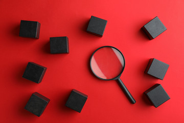 Black cubes and magnifier glass on red background, flat lay. Find keywords concept