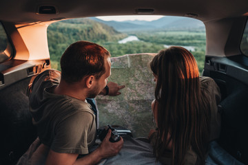 Happy Young Couple Lying in the Trunk of Their Car Enjoying Roadtrip, Man and Woman Using Map