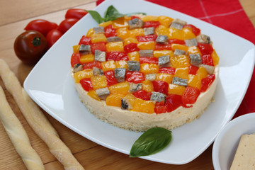 Salty cheesecake with ricotta cheese, red and yellow peppers and mackerel fish and basil on a plate on a wooden table 

