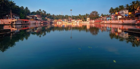 Fototapeta na wymiar Gokarna, Karnataka, Colorful indian houses, bright orange-striped temple tank on the bank of sacred lake Koti Teertha. The city is a holy pilgrimage site for Hinduists