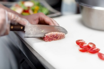 the chef beautifully cuts with his hand with a sharp knife pieces of fish sprinkled with sesame seeds on a white board in a restaurant to prepare food