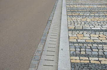 the edge of the road is drained by longitudinal channels of granite grids with gray slits at the...