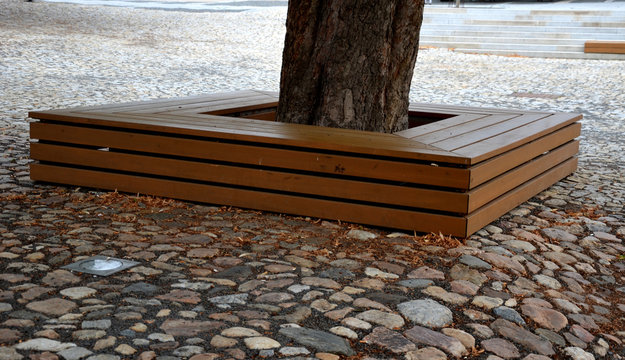 paving gray brown beige color of natural stone boulders of irregular shapes and colors. Benches around a square and rectangular tree lined with wood on a staircase