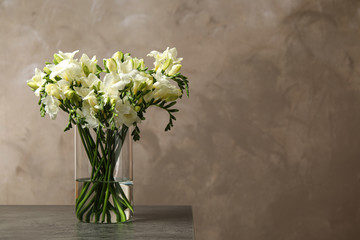 Beautiful freesia flowers in vase on grey table. Space for text