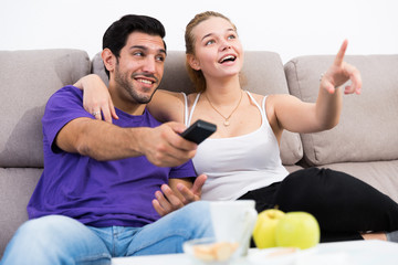 Fototapeta na wymiar Loving young couple sitting on sofa at home watching TV