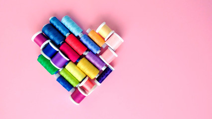 Flat lay composition of sewing threads in the shape of a heart on color pink background. Space for...
