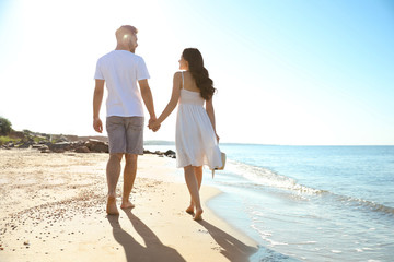 Fototapeta na wymiar Happy young couple walking on beach near sea. Honeymoon trip