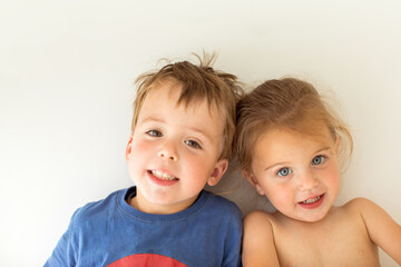 Adorable brother and sister smiling and looking at camera while leaning on white wall