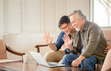 Elderly and technology concept, Happiness senior asian father and adult son using laptop talking on video call in living room