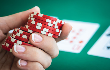 Poker chips in woman hand on playing cards background