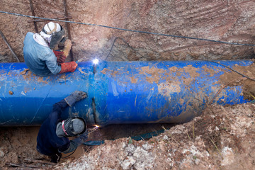 Workers weld large pipes plumbing water system underground at construction site.