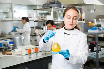 Young female lab technician working with reagents in test tubes during chemical experiment..