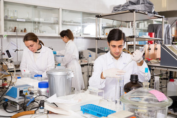 Intelligent student performing experiments in university laboratory, using mechanical lab pipette for mixing chemicals..