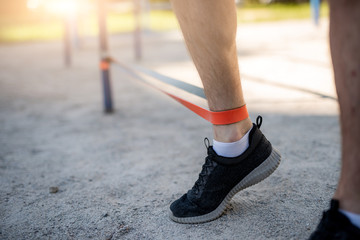 Fototapeta na wymiar Male legs training with elastic rubber outdoors, close up