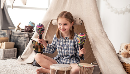 Happy little girl playing on wooden maracas in kids room decorated with ethnic drums and wigwam © Ievgen Skrypko