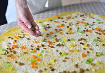 woman's hand sprinkles the dough with candied fruits and raisins
