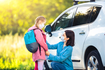 Daughter and mother in masks before going back to school on car parking