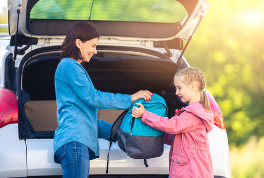 Mother giving backpack to daughter from car trunk before school
