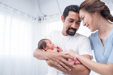 Fototapeta premium smiling mother and father holding their newborn baby at home..portrait of happy family at home, young parents holding on hands little sweet newborn baby, love and happiness concept.