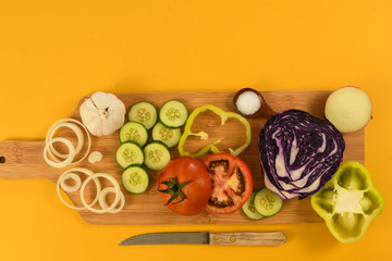 Table with tomato, cucumbers, cabbage, onion, garlic, knife, on yellow background. Top view.